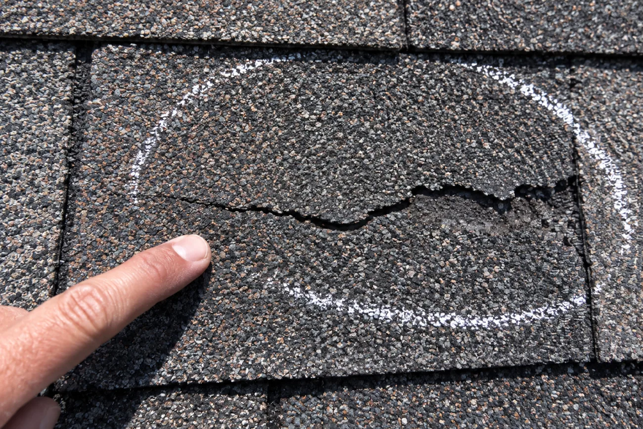 Cracked asphalt shingle circled with a chalk mark to document hail damage