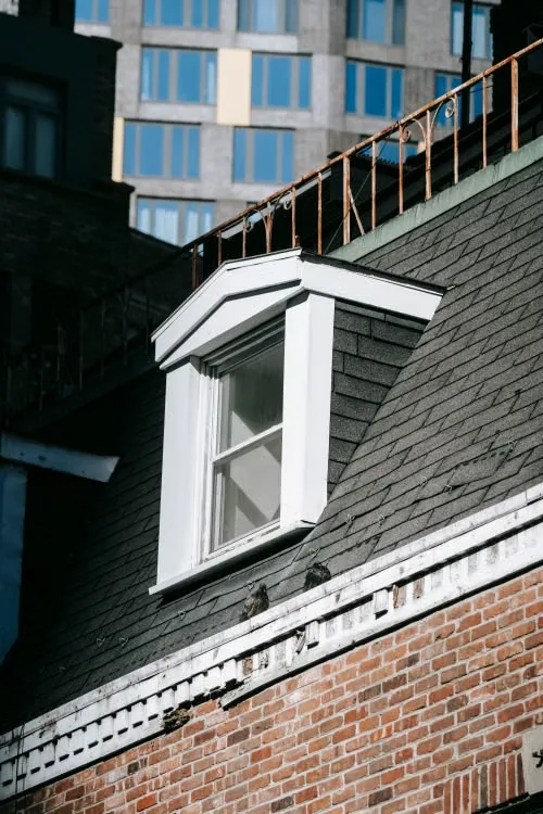 Attic window set into an asphalt shingle roof on an urban home